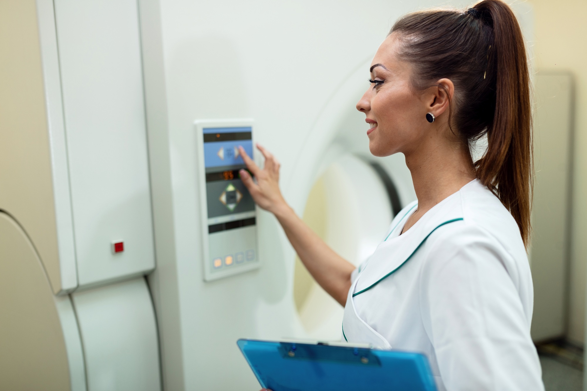 Smiling medical technician pressing control buttons on PET scan machine.