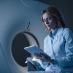 serious doctor looking at digital tablet with x-ray diagnosis while sitting near ct scanner