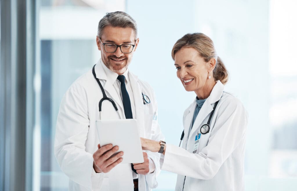 Medical, doctors and healthcare professionals working together on a digital tablet in a hospital. Portrait of a mature female and male doctor smiling and discussing diagnosis in a clinic.