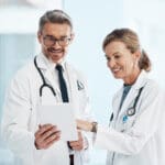 Medical, doctors and healthcare professionals working together on a digital tablet in a hospital. Portrait of a mature female and male doctor smiling and discussing diagnosis in a clinic.